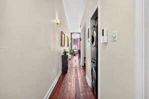 A hallway with a washing machine, a potted plant, and a dining area in the distance.