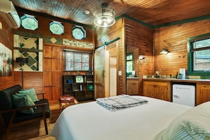 Ein gemütliches Zimmer im Chalet-Stil mit Bett, Schreibtisch, Stuhl und Küchenzeile.