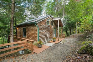 A rustic cabin with a wooden exterior, a wooden deck, and a gravel path leading to the entrance.