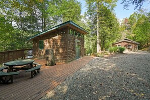 Une cabane en bois avec une table de pique-nique et un petit abri de jardin, située dans une zone boisée.