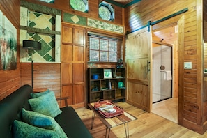Ein gemütliches Holzblockhaus-Interieur mit einer Couch, einer Leselampe, einem Bücherregal und einer Schiebetür zu einem Duschbereich.