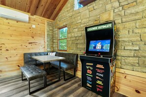 A cozy room with a stone wall, wooden ceiling, a gaming console, a table, and a bench.