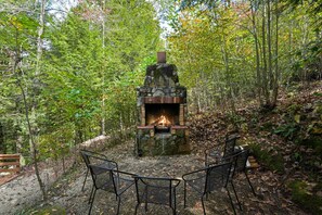 Ein steinerner Kamin, umgeben von einem Wald, mit Sitzgelegenheiten im Freien.