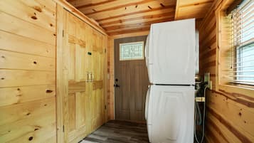 A wooden cabin interior with a refrigerator, wooden cabinets, and a small window with bars.