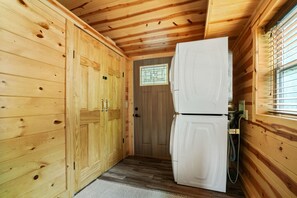 A wooden cabin interior with a refrigerator, wooden cabinets, and a small window with bars.