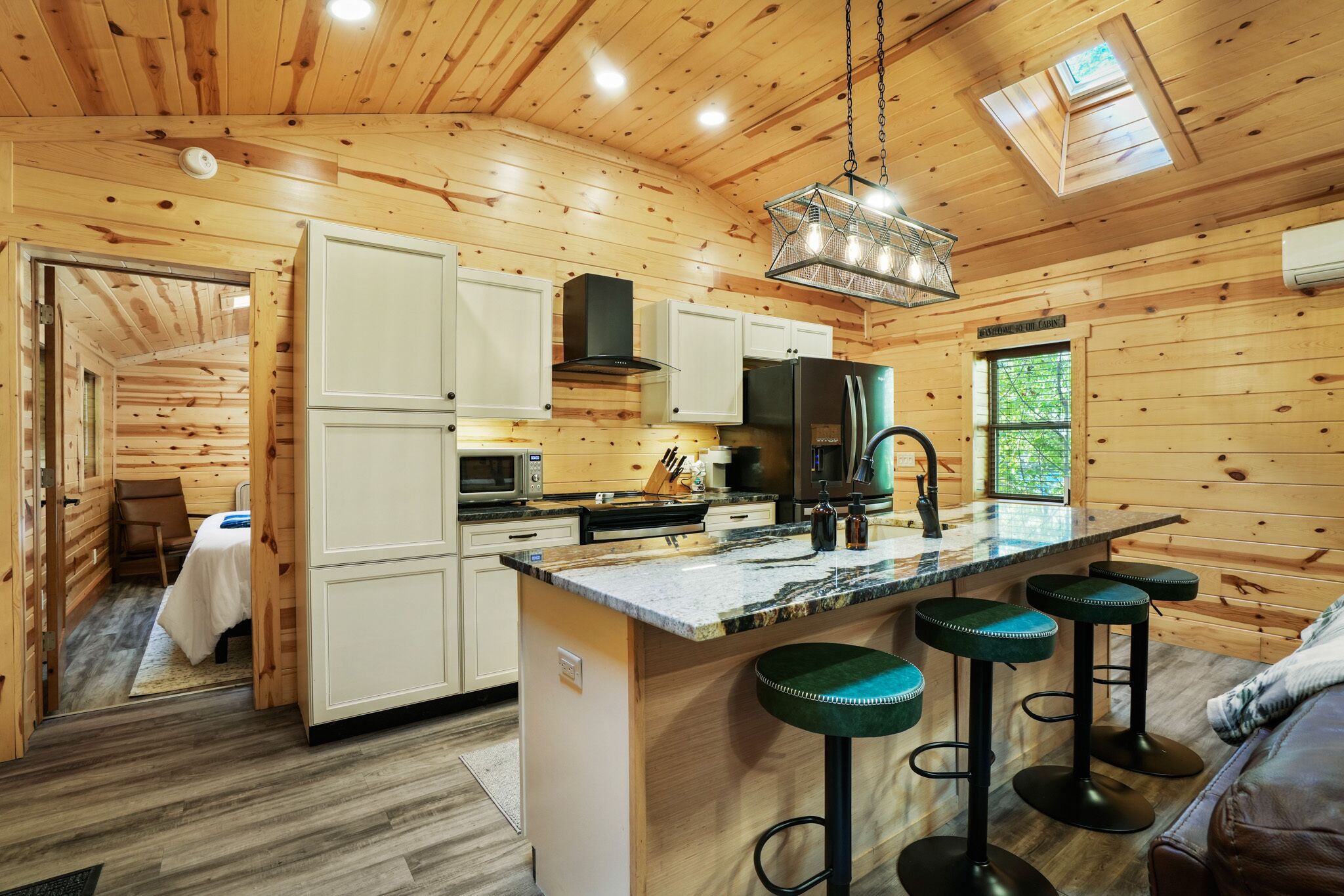 A wooden cabin interior with a kitchen, bar stools, and a dining area.
