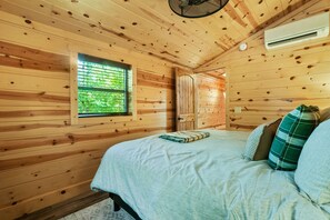 A wooden cabin room with a bed, a window, and an air conditioning unit.