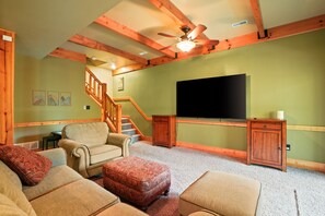 A living room with a sofa, ottoman, wooden staircase, and a flat-screen TV.