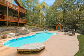 A wooden deck with a pool, a small cabin, and a stone feature.