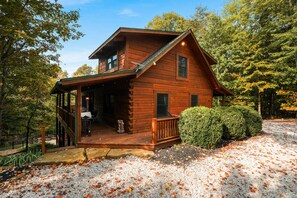 Une cabane en rondins avec un porche, une terrasse couverte et un jardin bien entretenu.