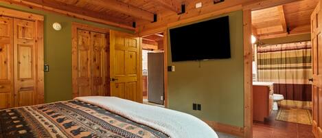 Une chambre dans une cabane en bois, avec un lit, une télévision et une salle de bain visible à travers une porte ouverte.