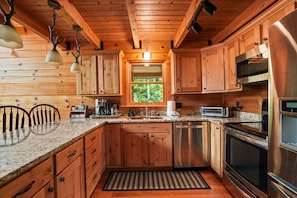 A kitchen with wooden cabinets, granite countertops, stainless steel appliances, and a window with a view of greenery.