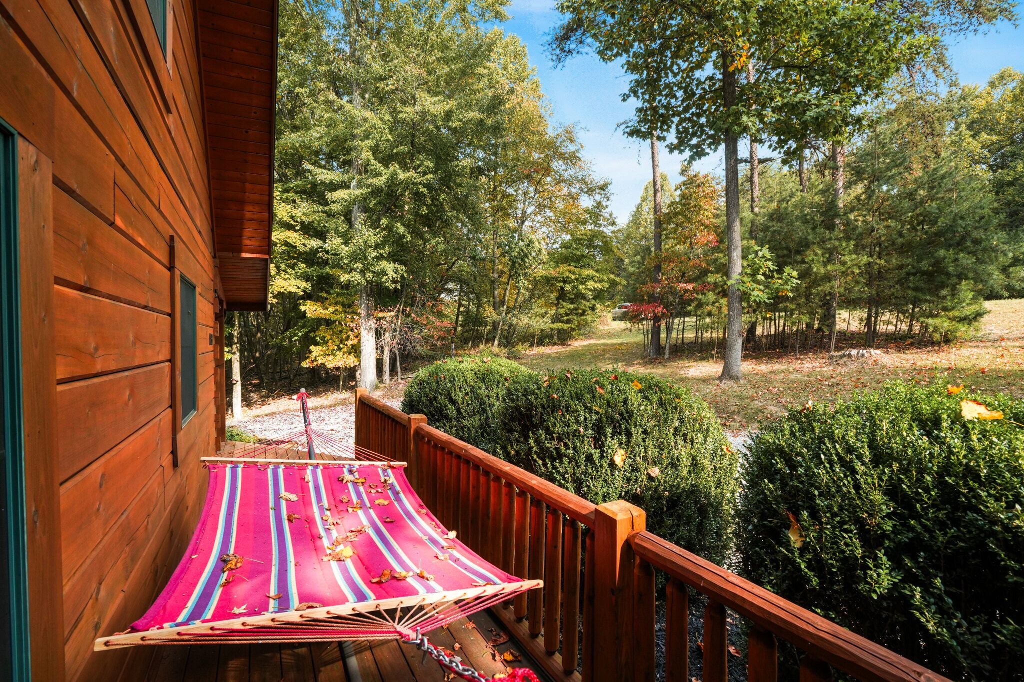 Une cabane en bois avec un hamac sur le porche, entourée d’arbres et d’une pelouse bien entretenue.