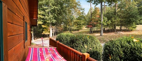 Une cabane en bois avec un hamac sur le porche, entourée d’arbres et d’une pelouse bien entretenue.