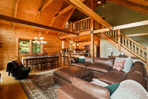 A spacious living room with a large brown leather sectional sofa, wooden dining table with chairs, and a staircase leading to an upper level. - Oasis Glen - Views, Pool, Hot Tub (Rockbridge)