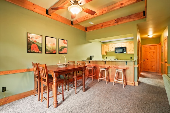 A dining area with a wooden table and chairs, a kitchen with wooden cabinets, and a ceiling fan.
