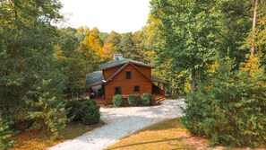 A wooden cabin surrounded by dense forest, with a gravel path leading to the entrance.