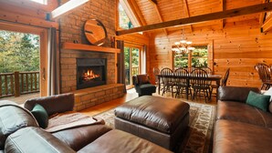 A log cabin interior with a fireplace, leather sofas, a dining area, and a wooden ceiling.