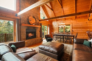 A log cabin interior with a fireplace, leather sofas, a dining area, and a wooden ceiling.