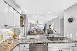 A modern kitchen with a central island, built-in appliances, and a dining area in the background. - GULF FRONT l BEACH VIEWS FOR DAYS!! l SEASONAL BEACH SETUP INCLUDED! (Santa Rosa Beach)