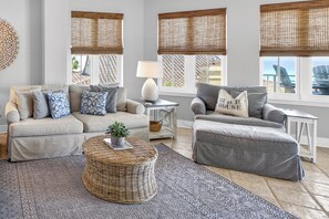 A living room with two sofas, a round wicker coffee table, a lamp, and a view of the outdoors through large windows with bamboo blinds. - GULF FRONT l BEACH VIEWS FOR DAYS!! l SEASONAL BEACH SETUP INCLUDED! (Santa Rosa Beach)