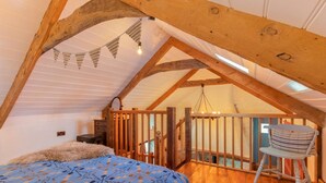 A cozy attic bedroom with a sloped ceiling, wooden beams, a bed with patterned bedding, a chair, and a small table.
