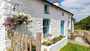 A white stone house with blue shutters, a wooden fence, and a flower basket.