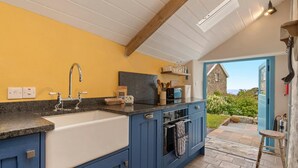 A kitchen with a large island, a sink, and a view of the garden through an open door.