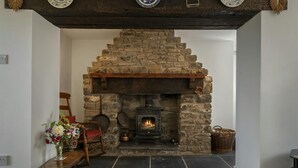 Una chimenea de piedra con repisa de madera, un banco con un jarrón de flores y una cesta de mimbre.