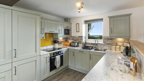 Una cocina moderna con gabinetes verde claro, una encimera de mármol y vistas al exterior a través de una ventana.