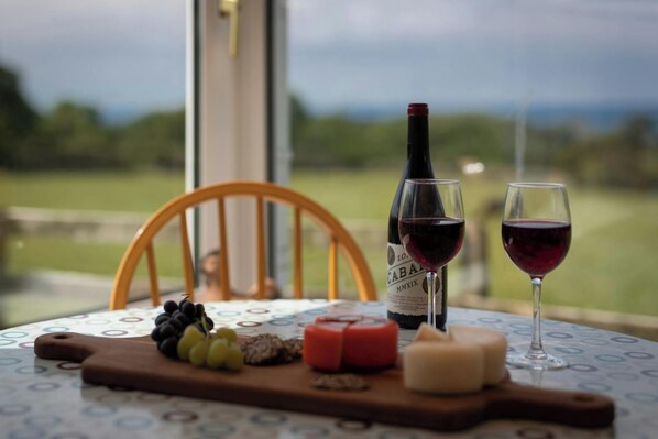 A table with a bottle of wine, two glasses of wine, a wooden board with grapes, cheese, and a candle.