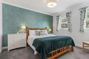 A bedroom with a wooden bed, white nightstands, a green blanket, and floral curtains.