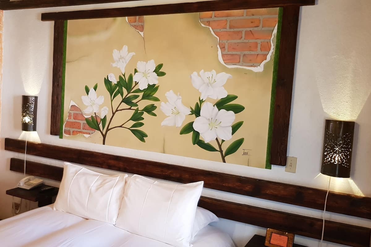 A hotel room with a bed, a nightstand, a phone, and a wall-mounted light fixture.