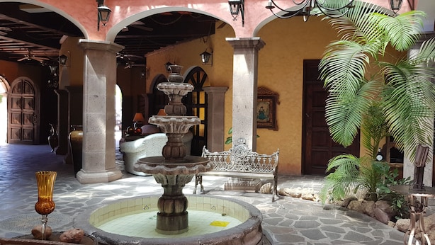 A courtyard with a stone fountain, a bench, and a potted plant. - Posada de las Flores Loreto (Loreto)
