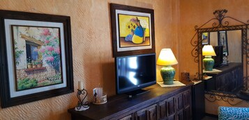 Una pared con dos cuadros enmarcados, un televisor de pantalla plana, una lámpara y un espejo.