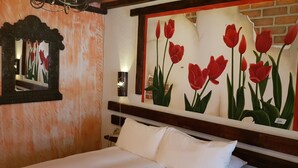 A hotel room with a bed, a nightstand, a mirror, and a wall with a red tulip painting. - Posada de las Flores Loreto (Loreto)