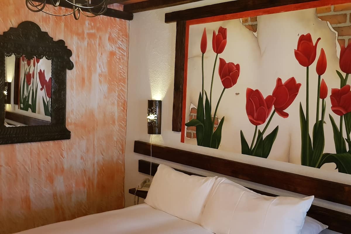 A hotel room with a bed, a nightstand, a mirror, and a wall with a red tulip painting.