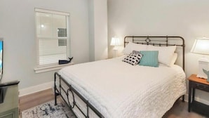 A bedroom with a bed, bedside tables, a window with blinds, and a television on a stand. - Gulf Front 3 Bedroom Condo in Mexico Beach at The Vue (Mexico Beach)