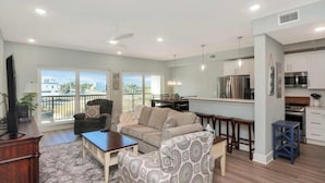 A spacious living room with a sofa, coffee table, and TV, a balcony with a view, and a modern kitchen with stainless steel appliances. - Gulf Front 3 Bedroom Condo in Mexico Beach at The Vue (Mexico Beach)