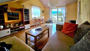 Un accogliente soggiorno con divano, tavolino e TV su un mobile in legno. Sul balcone, tavolo e sedie offrono uno spazio all'aperto.