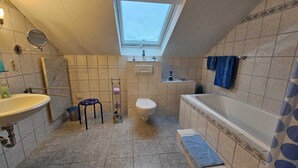 Un bagno compatto con finestra a lucernario, lavandino, WC e vasca da bagno.