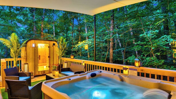A hot tub with a wooden deck, wicker chairs, and a view of a forest.