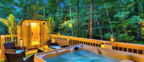 Een hottub met een houten terras, rieten stoelen en uitzicht op een bos.