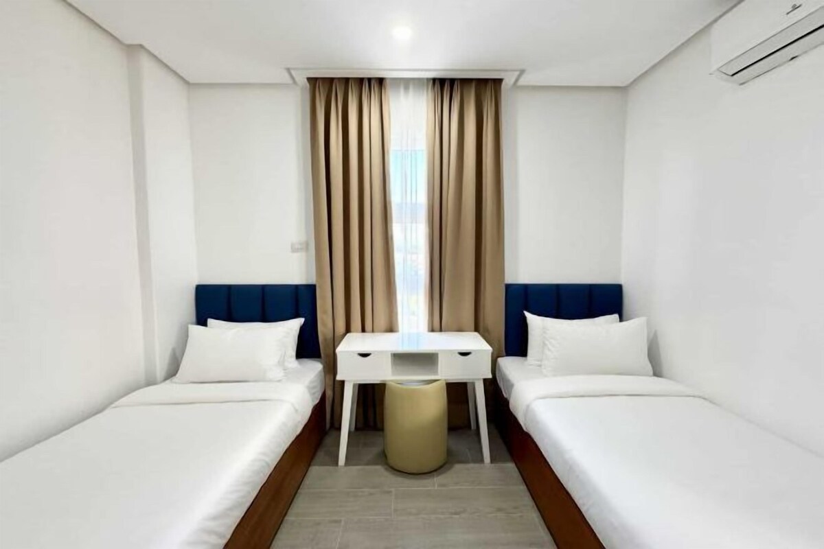 A hotel room with two single beds, a small desk, and a window with curtains.