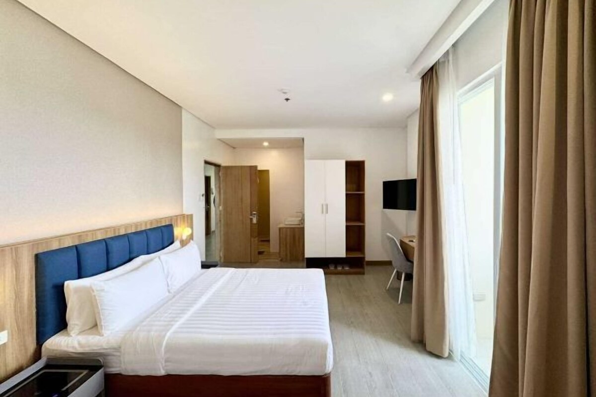 A hotel room with a large bed, a desk, a chair, and a TV.