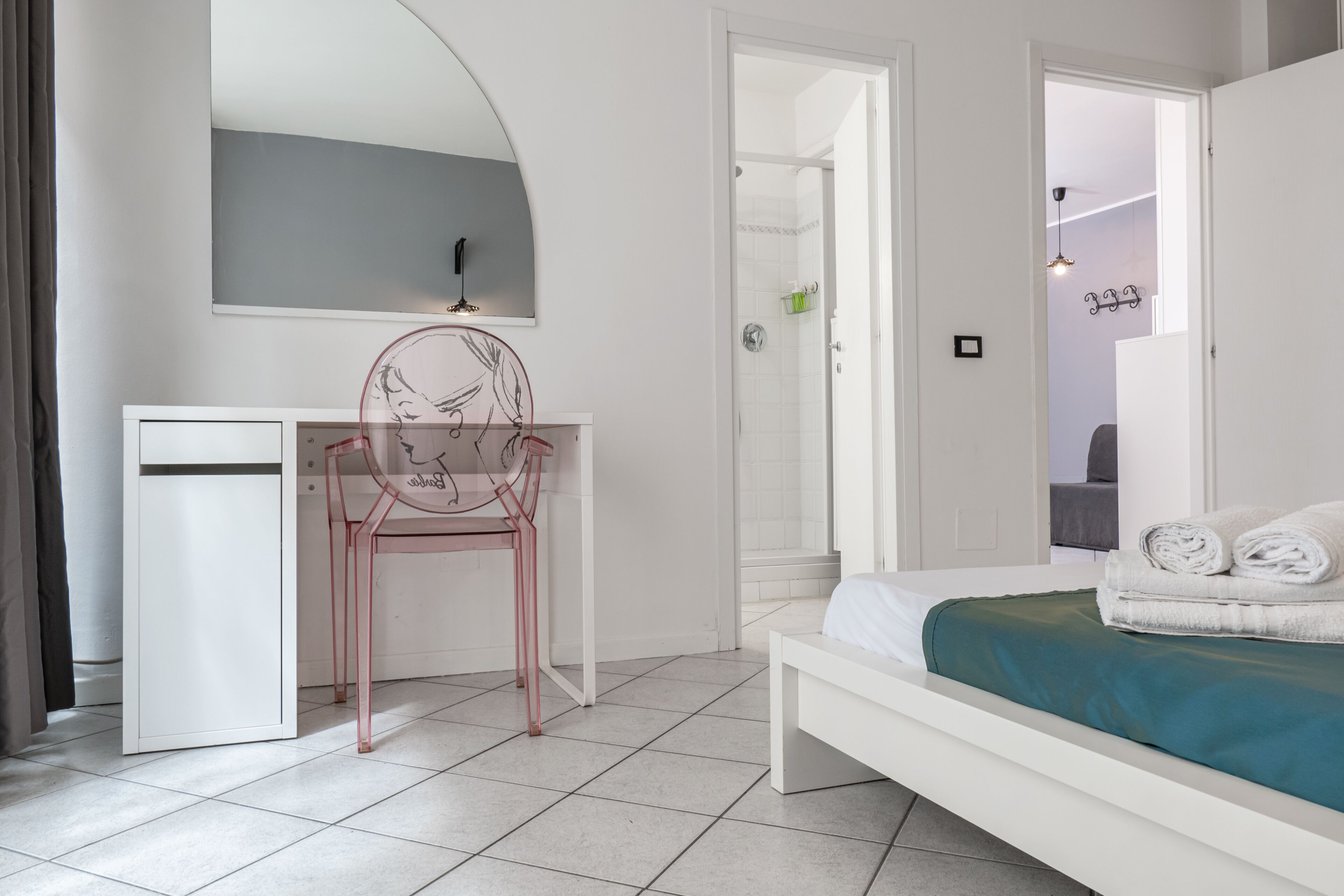 A bedroom with a bed, a desk, a chair, a mirror, and a shower area.