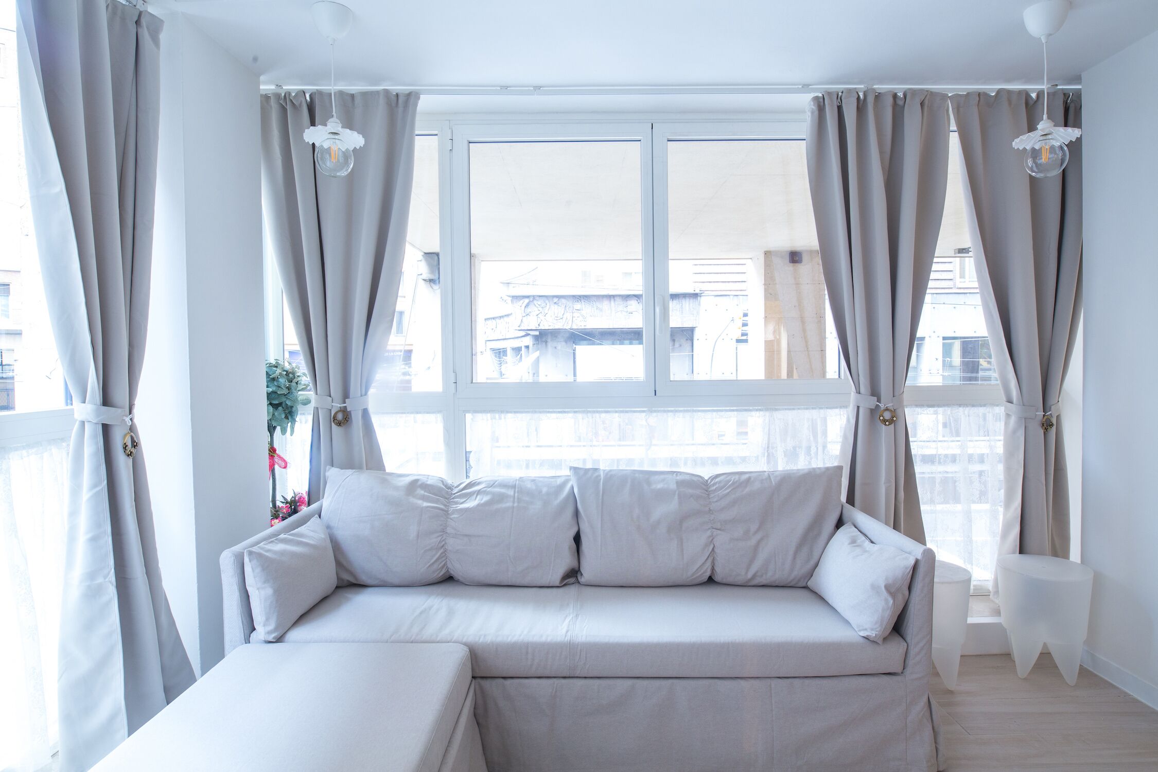 A modern bedroom with a large window, a sofa bed, and curtains.