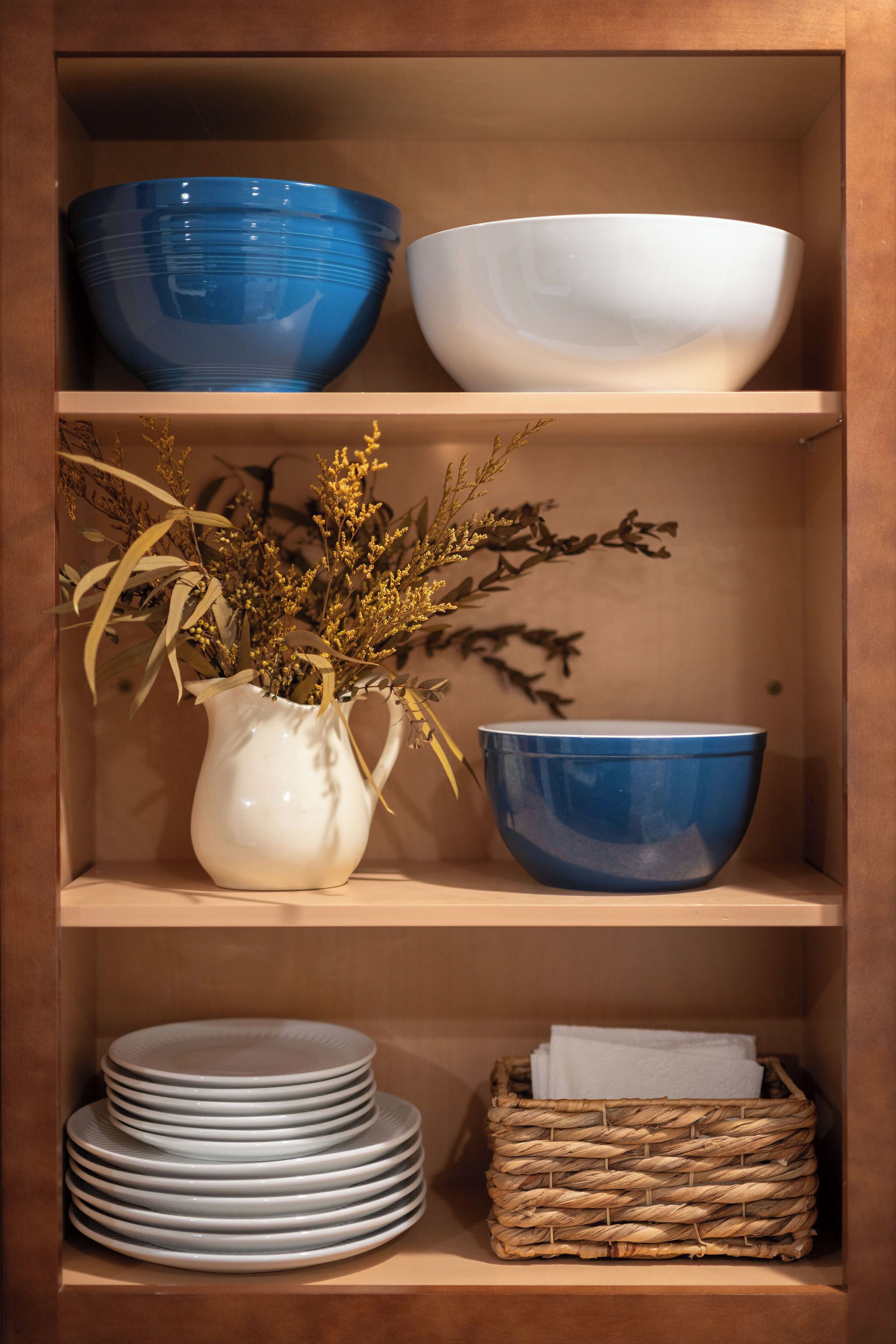 A wooden shelf with bowls, a vase with dried plants, and stacked plates.