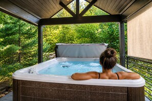A hot tub with a wooden deck and a view of trees.