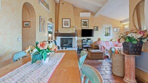A dining area with a wooden table, chairs, a fireplace, and a television. - Villa 'La Mignonette' with Sea View, Private Garden and Wi-Fi (Cavalaire-sur-Mer)